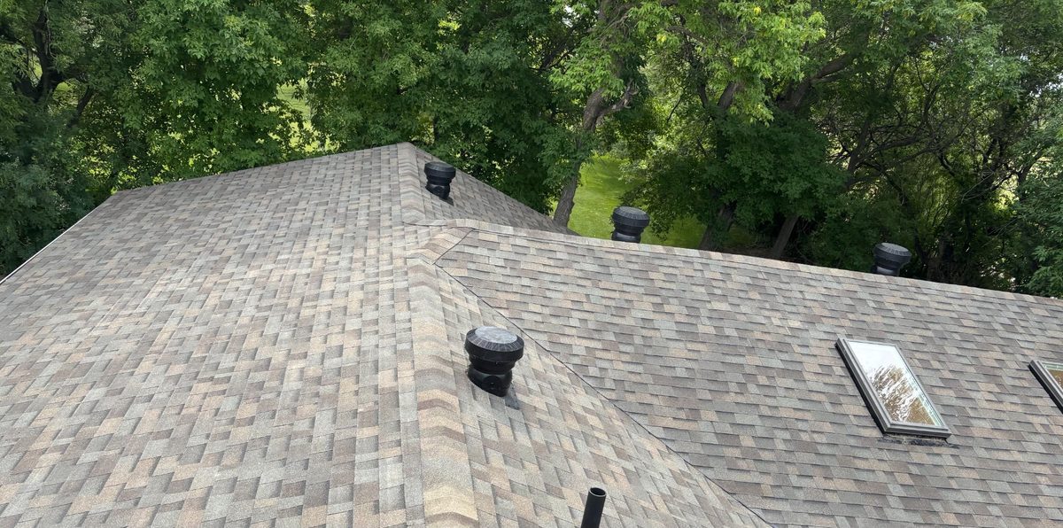 Drone view of completed architectural shingle roof with skylight and turbine vents surrounded by green canopy in Saskatchewan