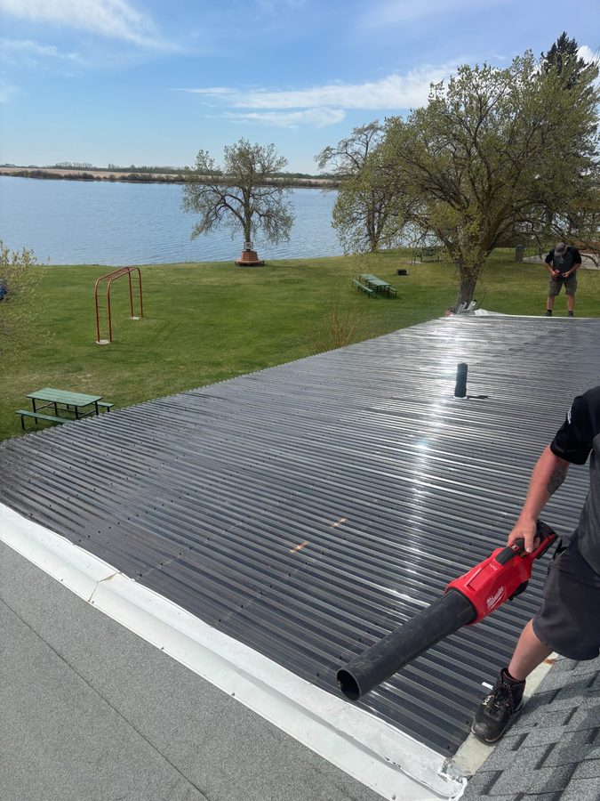 Metal roof installation at lakeside property in rural Saskatchewan with crew member using Milwaukee blower